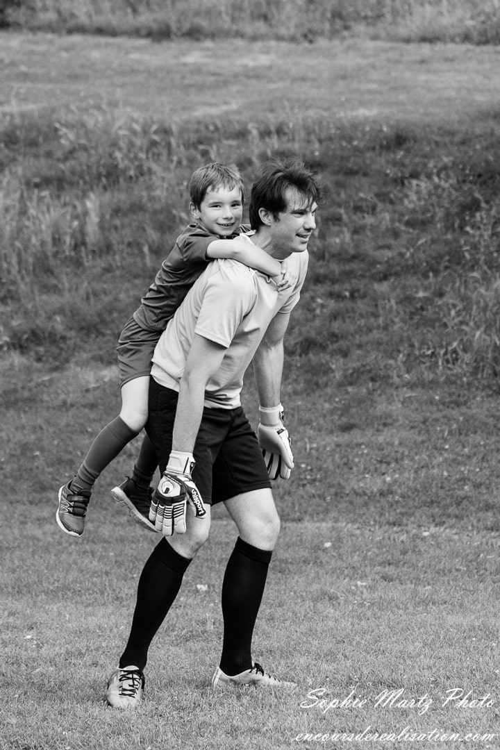 photo d'un père et son fils sur les épaules en train de jouer au foot